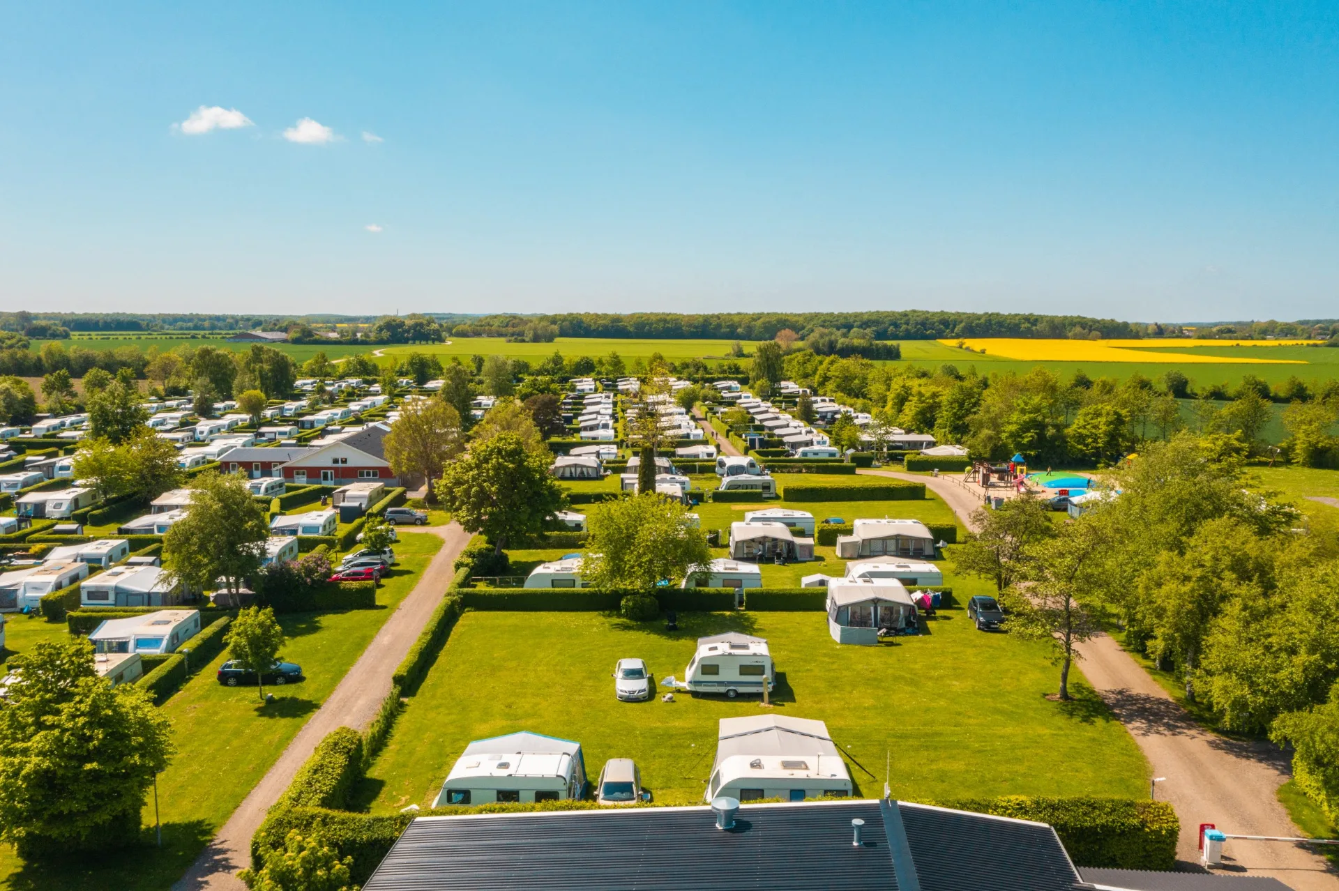 Luftfoto af Lægårdens Camping i Karise — campingvogne, fastliggerpladser, reception og legeplads omgivet af marker og rapsmarker